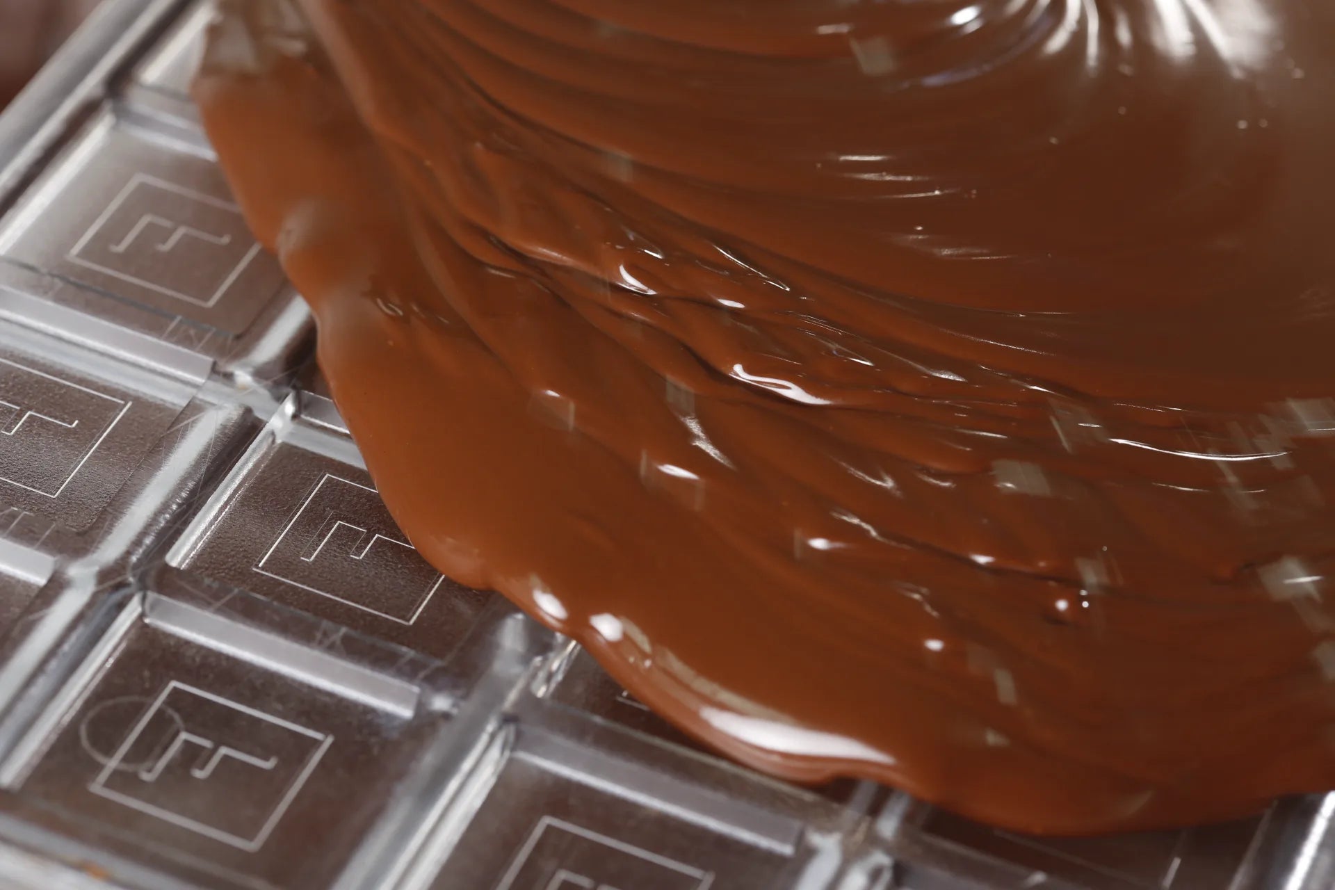 Melted milk chocolate pouring over a clear mold stamped with the Franceschi F