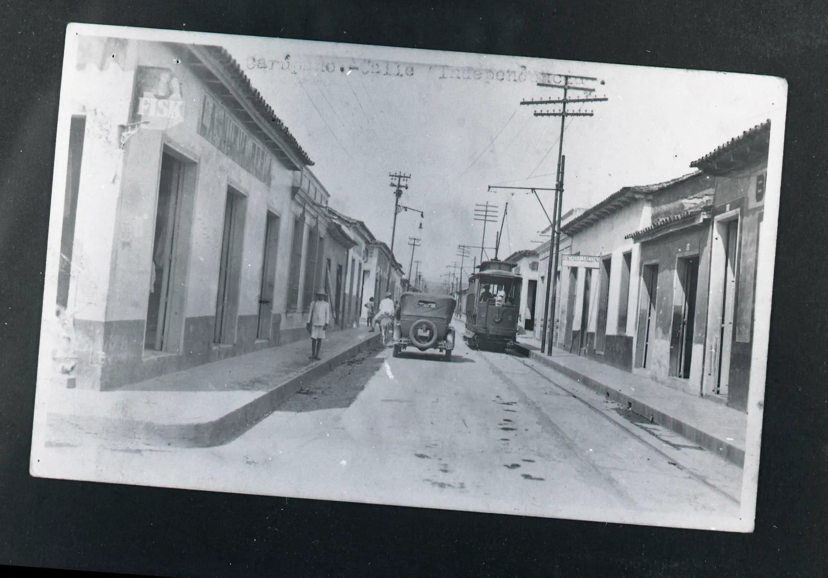 Old photograph of a Carúpano street with a tram and an early car