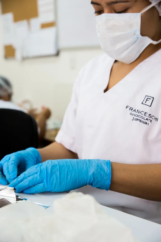 A Franceschi team member in a mask and gloves wrapping chocolate